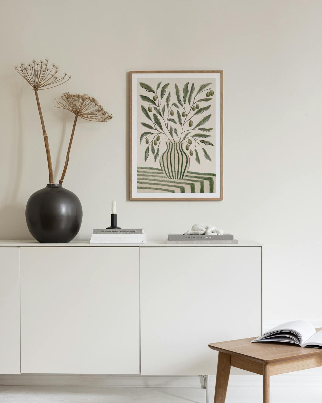 Affiche dun bouquet de branches dolivier dans un vase rayé vert, accrochée au-dessus dun bureau en bois clair.