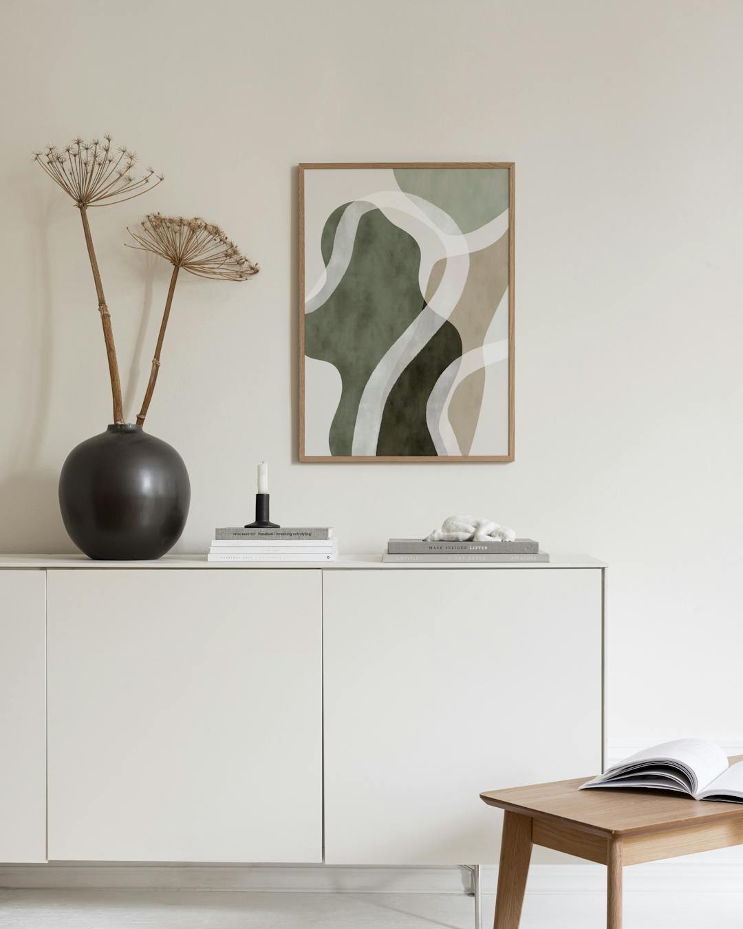 Affiche aux formes organiques vert olive, beige avec des lignes blanches, accrochée au-dessus dun pouf.
