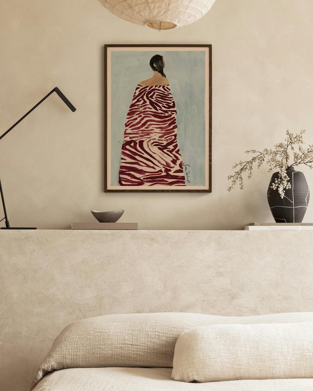 Affiche dune femme à la robe zébrée rouge et blanc, au-dessus dun canapé beige dans un salon moderne.